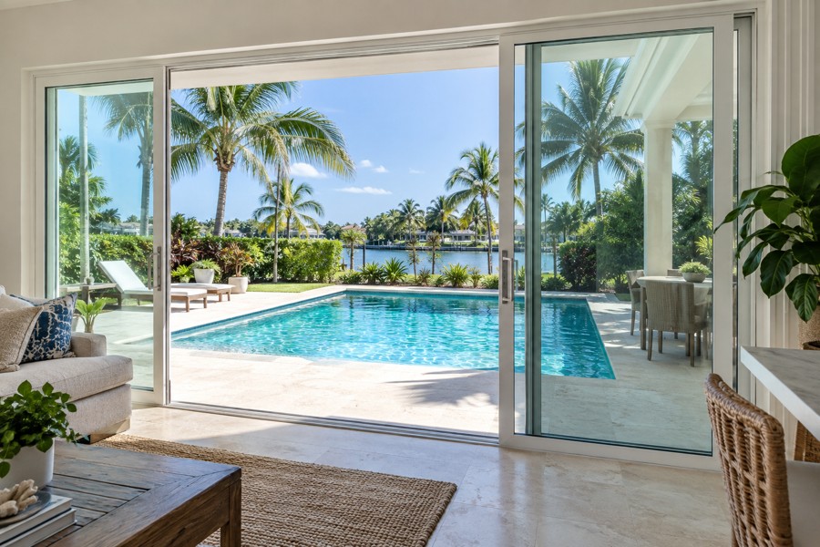 Sliding glass patio doors with one panel open onto a blue swimming pool and tropical landscaping